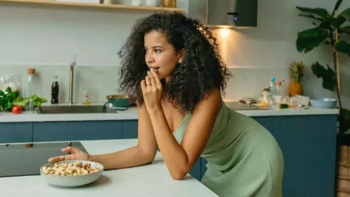 Femme dans une cuisine en train de grignoter, illustrant le lien entre émotions, envies alimentaires et alimentation émotionnelle.