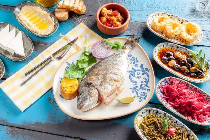 Table méditerranéenne avec poisson grillé, féta, houmous, olives et légumes marinés